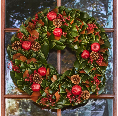 magnolia wreath for pine cones and red berries hanging on a door.