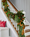 Decorative garland with greenery and brown leaves on a staircase with a red pillow.
