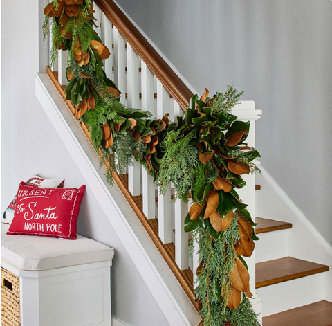 Decorative garland with greenery and brown leaves on a staircase with a red pillow.