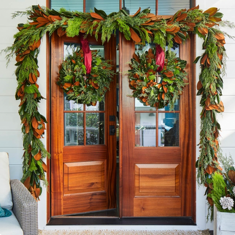 Decorative wreaths and garlands on a wooden door with festive greenery.