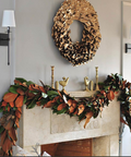 Decorative wreath and garland on a fireplace mantel with gold accents.