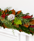 Decorative Christmas garland with greenery, red berries, and white pinecones on a white background.
