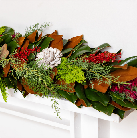 Decorative Christmas garland with greenery, red berries, and white pinecones on a white background.