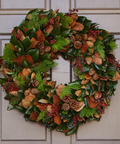 Decorative wreath with green leaves, brown berries, and pinecones on a door.