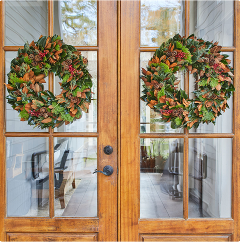 Two festive wreaths on a wooden door with glass panels.
